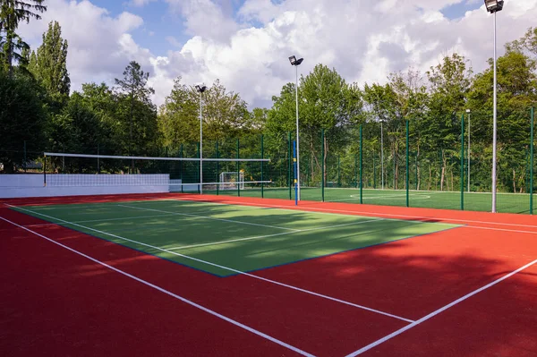 stock image A sports field in a park with artificial grass and a stretched net against the background of green trees, with the morning rays of the sun, at dawn