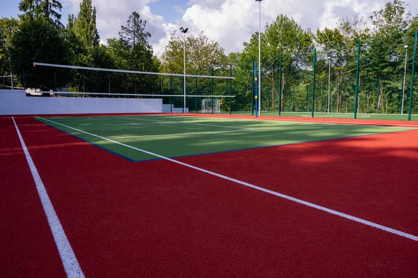 Parktaki bir spor sahasında yapay çimenler ve yeşil ağaçların arka planında gerilmiş bir ağ, güneşin sabah ışıklarıyla, şafakta