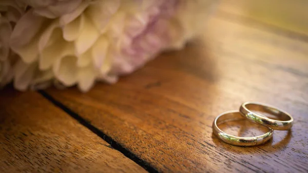 Μια Ξύλινη Επιφάνεια Βέρες Γάμου Και Ένα Δαχτυλίδι Κοντά Λουλούδια — Φωτογραφία Αρχείου