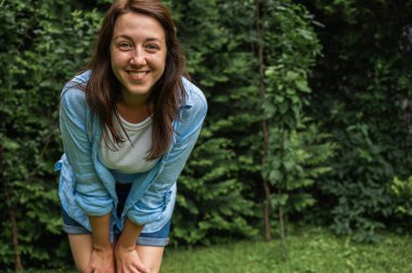 Genç bir kadın duygusaldır, düşüncelidir ve yazın yeşilliğin arka planına karşı parktan uzağa bakar. Yana doğru bak.