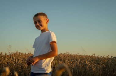 Beyaz tişörtlü küçük bir çocuğun portresi, akşam üstü Ukrayna 'da bir buğday tarlasında, Lviv yakınlarında, yazıtlar için bir yer. Batıda huzurlu bir gökyüzü