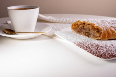 Elma ve tarçınla doldurulmuş bir parça lezzetli turta, kahve telvesi ve hafif arka planlı bir tabakta. Yazmak için yer var. Görüntüyü kapat