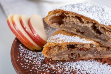 Paired pieces of delicious strudel stuffed with apples and cinnamon on a light plate on a light background. Place for writing. Close up view. Homemade Ukrainian pastries clipart