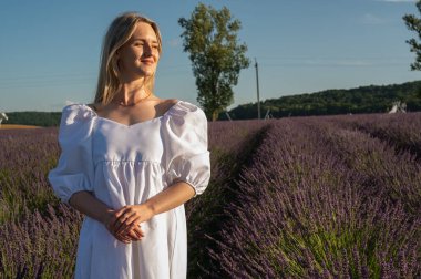 Lviv, Ukrayna yakınlarındaki lavanta tarlaları. Yazın açan lavanta. Beyaz yaz elbiseli bir kız lavanta tarlalarında yürüyor ve elleriyle lavanta çiçeklerine dokunuyor. Seçici odak