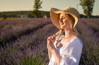 Beyaz elbiseli, lavanta tarlasında şapkalı genç ve güzel bir kız yan tarafa bakıyor. Yazı için yer