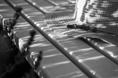 Siyah beyaz fotoğraf, gölge, bir kadının hasır şapkası beyaz ahşap bir bankta yatıyor, üzerinde bir demet lavanta yatıyor, gün batımı ışınlarında. Yazmak için yer, arkaplan