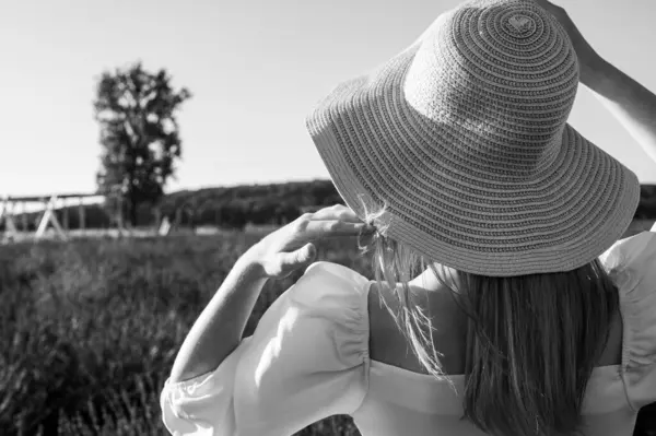 black and white classic photo, young beautiful girl in a white dress in a hat on a lavender field, looking to the side. Place for writing
