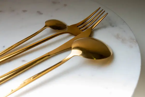 dessert fork, spoon, knife of golden color on a light surface