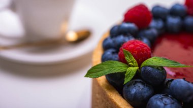 Taze böğürtlen, yabanmersini, ahududu ve nane yapraklarıyla süslenmiş cheesecake 'in yakın çekimi. Şekerlemeler, pişirme, parlak renkler