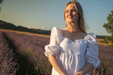 Lviv, Ukrayna yakınlarındaki lavanta tarlaları. Yazın açan lavanta. Beyaz yaz elbisesi içinde bir kızın portresi, gülümseyen lavanta tarlaları, gün batımı. Seçici odak