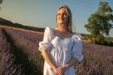 Lviv, Ukrayna yakınlarındaki lavanta tarlaları. Yazın açan lavanta. Beyaz yaz elbisesi içinde bir kızın portresi, gülümseyen lavanta tarlaları, gün batımı. Seçici odak