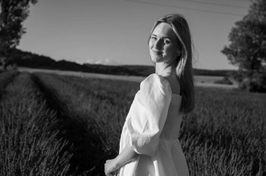 Beyaz yaz elbiseli bir kızın siyah beyaz portresi lavanta tarlalarında yürüyor. Lviv, Ukrayna yakınlarındaki lavanta tarlaları. Yazın açan lavanta. Gün batımı. Seçici odak