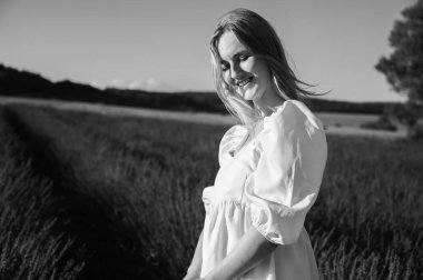 Beyaz yaz elbiseli bir kızın siyah beyaz portresi lavanta tarlalarında yürüyordu. Lviv, Ukrayna yakınlarındaki lavanta tarlaları. Yazın açan lavanta. Gün batımı. Seçici odak