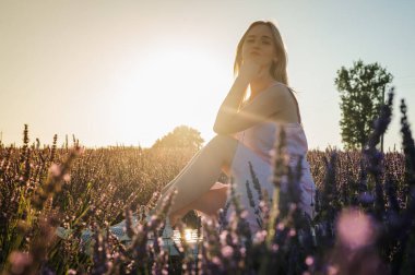 Gün batımının ışınlarında, beyaz elbiseli rahat bir genç kızın yan portresi, beyaz bir bankta oturuyor, temiz hava soluyor, güneşli bir günde lavanta tarlasında oturuyor, uzaklara bakıyor, düşünüyor. Yazmak için bir yer