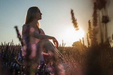 Gün batımının ışınlarında, beyaz elbiseli rahat bir genç kızın yan portresi, beyaz bir bankta oturuyor, temiz hava soluyor, güneşli bir günde lavanta tarlasında oturuyor, uzaklara bakıyor, düşünüyor. Yazmak için bir yer