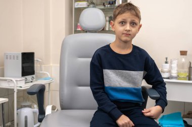 Küçük bir çocuk, sarışın bir genç, otolaryngolojistin ofisinde oturuyor, sınavı bekliyor, endişeli ama gülümsüyor. Yazı için yer