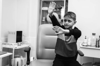 Siyah ve beyaz bir fotoğraf, küçük bir çocuk, sarışın bir genç, muayene için otolargologun ofisinde oturuyor, korkuyor, elleriyle itiyor, korku. Yazacak bir yer