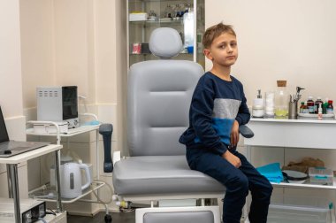 Küçük bir çocuk, sarışın bir genç, otolaryngolojistin ofisinde oturuyor, sınavı bekliyor, endişeli ama gülümsüyor. Yazı için yer