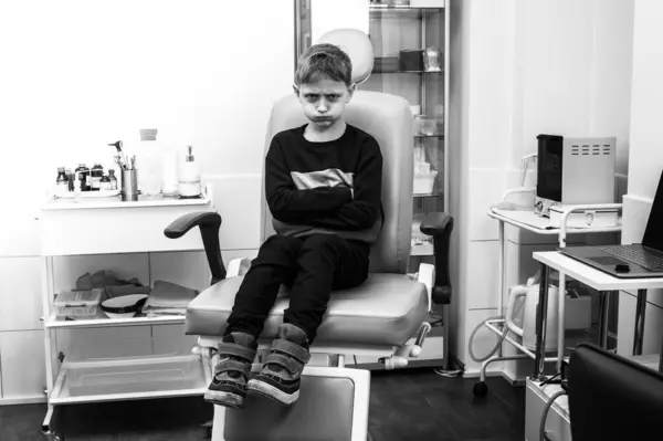 Black and white photo, little boy, fair-haired teenager, sitting in otolaryngologist\'s office, waiting for examination, worried, emotional, but smiling, health care. A place for writing