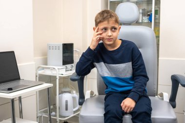 Küçük bir çocuk, sarışın bir genç, otolaryngolojistin ofisinde oturuyor, sınavı bekliyor, endişeli ama gülümsüyor. Yazı için yer