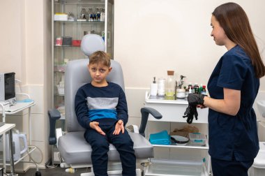 Küçük bir çocuk, sarışın bir genç, otolaringolojistin ofisinde oturuyor, doktorda kulak muayenesi yaptırıyor, endişeli, duygusal, ama gülümsüyor. Fiziksel muayene.