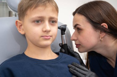 Küçük bir çocuk, sarışın bir genç, otolaringolojistin ofisinde oturuyor, doktorda kulak muayenesi yaptırıyor, endişeli, duygusal, ama gülümsüyor. Fiziksel muayene.