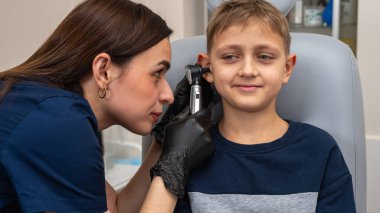 Küçük bir çocuk, sarışın bir genç, otolaringolojistin ofisinde oturuyor, doktorda kulak muayenesi yaptırıyor, endişeli, duygusal, ama gülümsüyor. Fiziksel muayene.