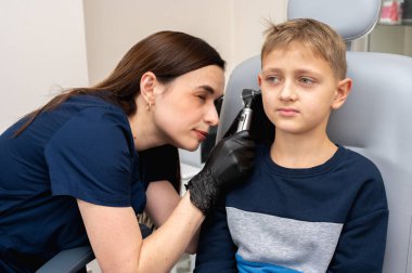 Küçük bir çocuk, sarışın bir genç, otolaringolojistin ofisinde oturuyor, doktorda kulak muayenesi yaptırıyor, endişeli, duygusal, ama gülümsüyor. Fiziksel muayene.