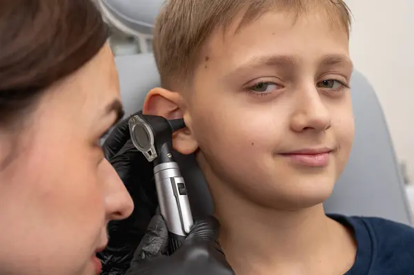 little boy, fair-haired teenager, sitting in an otolaryngologist\'s office, having an ear examination at the doctor\'s, worried, emotional, but smiling. Physical examination