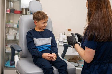 Bir klinikte otoskoplu bir doktor tarafından muayene edilen sarışın bir çocuğun portresi, duygusal bir şekilde sandalyede oturuyor. Yakın çekim, tıbbi muayene.