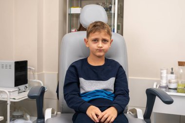 Bir klinikte otoskoplu bir doktor tarafından muayene edilen sarışın bir çocuğun portresi, duygusal bir şekilde sandalyede oturuyor. Yakın çekim, tıbbi muayene.