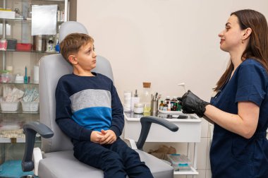 Bir klinikte otoskoplu bir doktor tarafından muayene edilen sarışın bir çocuğun portresi, duygusal bir şekilde sandalyede oturuyor. Yakın çekim, tıbbi muayene.