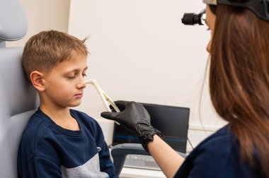 Burun muayenesi ve muayenesi, küçük çocuk, gülümseyen sarışın genç, otolaringolojistin ofisinde oturuyor, doktordaki burun deliklerini inceliyor, güvenen, duygusal, gülümseyen. Fiziksel muayene.