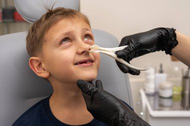 Burun muayenesi ve muayenesi, küçük çocuk, gülümseyen sarışın genç, otolaringolojistin ofisinde oturuyor, doktordaki burun deliklerini inceliyor, güvenen, duygusal, gülümseyen. Fiziksel muayene.