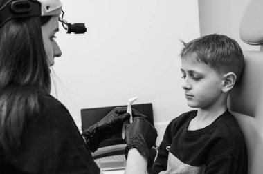 Burun muayenesi ve muayenesi, küçük çocuk, gülümseyen sarışın genç, otolargolojistin ofisinde oturuyor, doktordaki burun deliklerini inceliyor, güvenen, duygusal, gülümseyen.