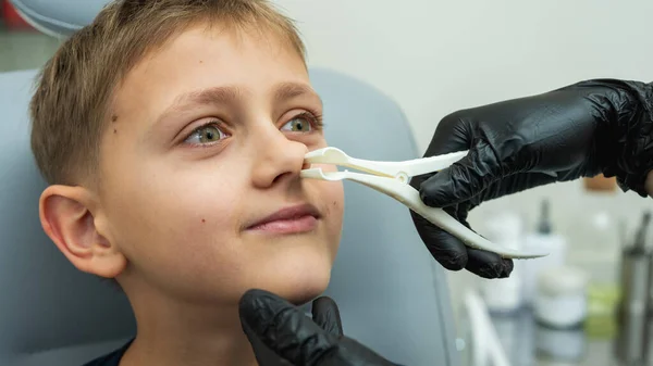 examination and examination of the nose, little boy, fair-haired teenager smiling, sitting in the otolaryngologist\'s office, examining the nasal passages at the doctor, trusting, emotional, smiling. Physical examination