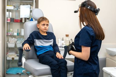 Küçük bir çocuk, sarışın bir genç, otolaringolojist ofisinde oturuyor, muayene, konsültasyon, doktorda muayene, duygusal ama gülümseyen. Fiziksel muayene.