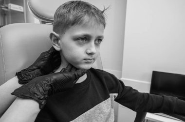 Boynun siyah ve beyaz muayenesi, üst çene sinüsleri, yüze masaj yapan küçük bir çocuk, sarışın bir genç endişeli, otoların muayenehanesinde oturuyor, doktor burun kemiğini inceliyor.