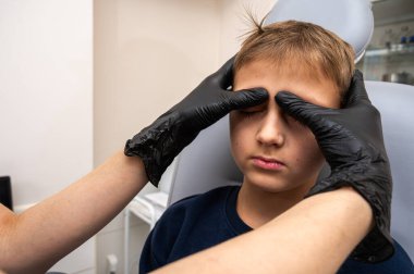 Boynun incelenmesi, üst çene sinüsleri, yüze masaj yapılması, küçük bir çocuk, sarışın bir genç, otolarngolojistin ofisinde otururken, doktor burun deliklerini ve boynu duygusal olarak inceler. Tedavi ilaçları