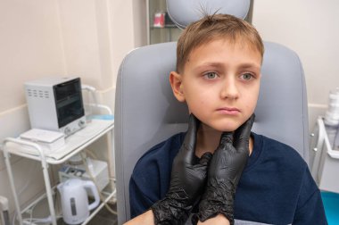 Boyun muayenesi, üst çene sinüsleri, yüze masaj, küçük bir çocuk, sarışın bir genç endişeli, otoların muayenehanesinde oturuyor, doktor burun kemiğini muayene ediyor.