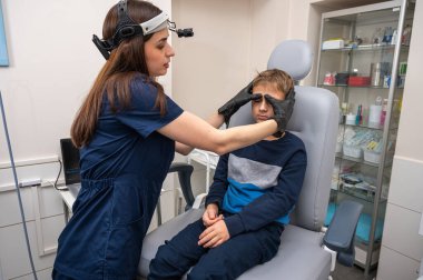 Boyun muayenesi, üst çene sinüsleri, yüze masaj, küçük bir çocuk, sarışın bir genç endişeli, otoların muayenehanesinde oturuyor, doktor burun kemiğini muayene ediyor.