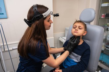 Boyun muayenesi, üst çene sinüsleri, yüze masaj, küçük bir çocuk, sarışın bir genç endişeli, otoların muayenehanesinde oturuyor, doktor burun kemiğini muayene ediyor.