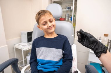 Boğaz muayenesi, küçük bir çocuk, sarışın bir genç, otolaringolojistin ofisinde oturuyor, doktor boğazını inceliyor, endişeli, duygusal, ama gülümsüyor. Fiziksel muayene.