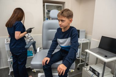 Küçük bir çocuk, sarışın bir genç, otolaringolojistin ofisinde oturuyor, doktorda kulak muayenesi yaptırıyor, endişeli, duygusal, ama gülümsüyor. Fiziksel muayene.