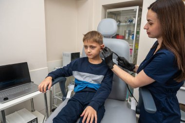 Küçük bir çocuk, sarışın bir genç, otolaringolojistin ofisinde oturuyor, doktorda kulak muayenesi yaptırıyor, endişeli, duygusal, ama gülümsüyor. Fiziksel muayene.