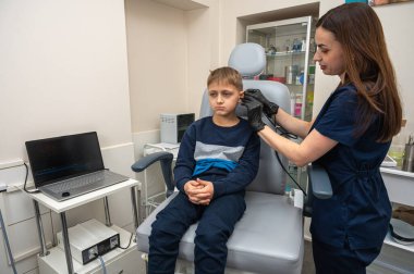 Küçük bir çocuk, sarışın bir genç, otolaringolojistin ofisinde oturuyor, doktorda kulak muayenesi yaptırıyor, endişeli, duygusal, ama gülümsüyor. Fiziksel muayene.