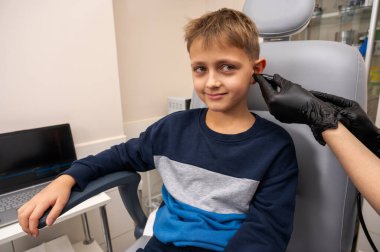 Küçük bir çocuk, sarışın bir genç, otolaringolojistin ofisinde oturuyor, doktorda kulak muayenesi yaptırıyor, endişeli, duygusal, ama gülümsüyor. Fiziksel muayene.