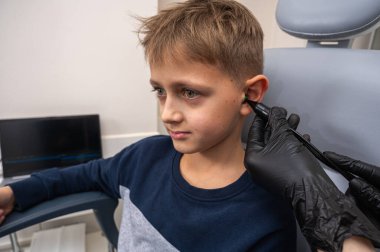 Küçük bir çocuk, sarışın bir genç, otolaringolojistin ofisinde oturuyor, doktorda kulak muayenesi yaptırıyor, endişeli, duygusal, ama gülümsüyor. Fiziksel muayene.