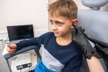 Küçük bir çocuk, sarışın bir genç, otolaringolojistin ofisinde oturuyor, doktorda kulak muayenesi yaptırıyor, endişeli, duygusal, ama gülümsüyor. Fiziksel muayene.