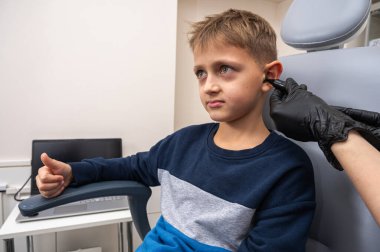 Küçük bir çocuk, sarışın bir genç, otolaringolojistin ofisinde oturuyor, doktorda kulak muayenesi yaptırıyor, endişeli, duygusal, ama gülümsüyor. Fiziksel muayene.